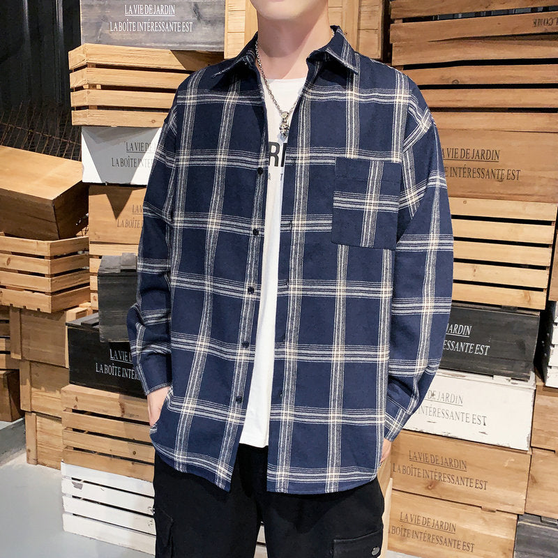 Person wearing a blue plaid shirt over a white shirt, standing in front of stacked wooden crates.