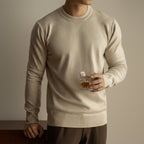 Man wearing a beige sweater holding a glass of whiskey against a neutral background