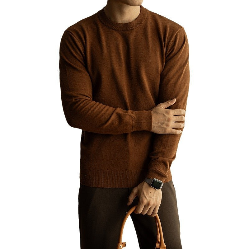 Person wearing a brown sweater with arms crossed, holding a brown leather bag on a white background