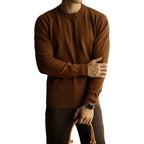Person wearing a brown sweater with arms crossed, holding a brown leather bag on a white background
