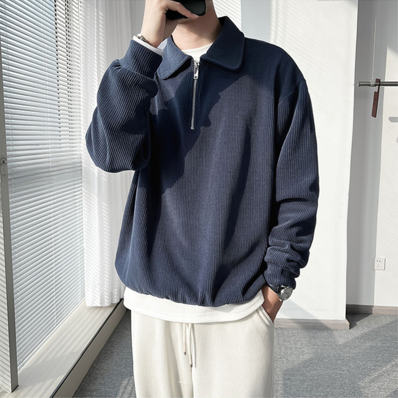 Person wearing a navy blue zip-up sweatshirt and white pants in an indoor setting.